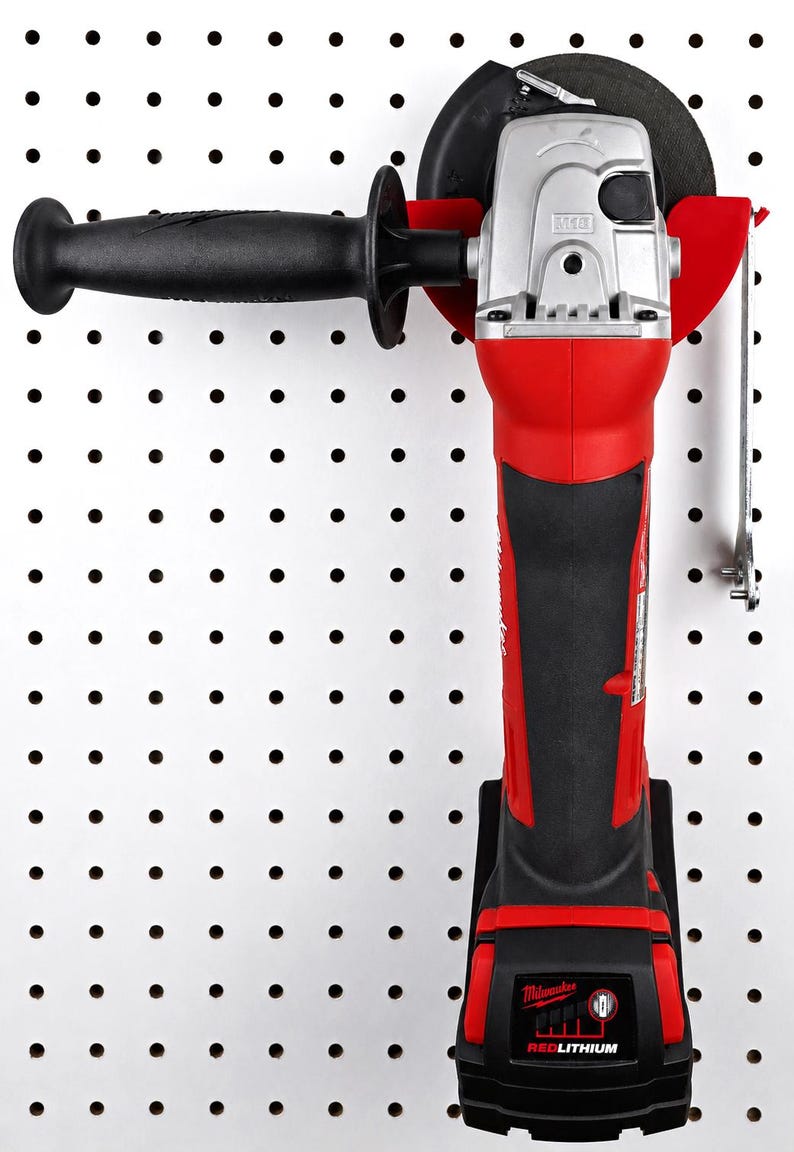May include: A red and black cordless angle grinder with a black handle and a silver motor housing. The grinder has a black grinding wheel and is labeled "Milwaukee" and "REDLITHIUM". It is mounted on a white pegboard.