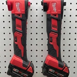 May include: Two red and black Milwaukee M18 cordless right angle drills. The drills are mounted on a white pegboard. The tools have a red head and base with black handles. The battery packs are labeled M18 REDLITHIUM XC 2.0.