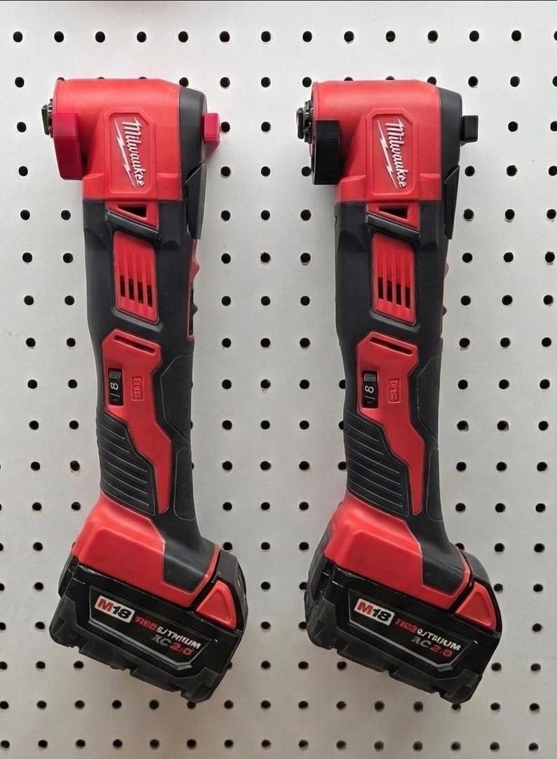 May include: Two red and black Milwaukee M18 cordless right angle drills. The drills are mounted on a white pegboard. The tools have a red head and base with black handles. The battery packs are labeled M18 REDLITHIUM XC 2.0.