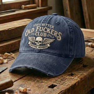 May include: A navy blue baseball cap with a distressed finish. The cap features the text "100% Bitter Old Fuckers Club" with a skull and wings emblem, and "Lifetime Member" on a banner.