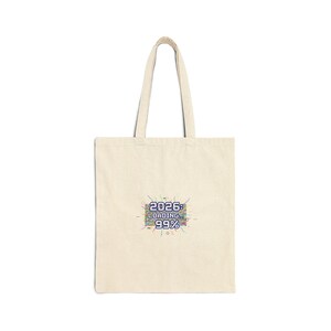 May include: Cream-coloured tote bag featuring the text "2026: LOADING... 99%" in a pixelated, multi-coloured design. The bag has a rectangular shape and two handles for carrying.