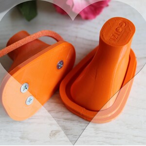 May include: Two bright orange plastic shoe heel replacements with a textured base and a vertical post. One piece shows two silver metal screws on the underside, while the other displays the embossed text GOIZ on the top surface of the heel.
