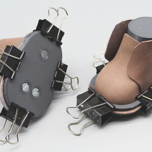 May include: Two brown leather shoe forms are being held together with binder clips. The forms are being used to create a shoe.