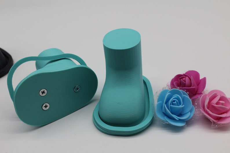 May include: Two turquoise blue 3D printed shoe forms with a base and a raised top. The shoe forms are on a white surface with three artificial flowers in pink and blue.