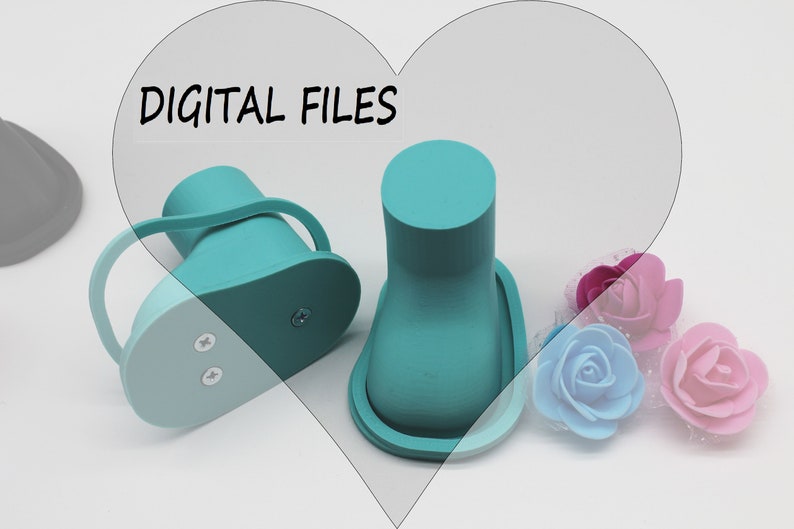 May include: Two teal blue 3D printed baby shoes with a strap on one shoe. The shoes are on a white surface with pink, blue, and purple artificial flowers.