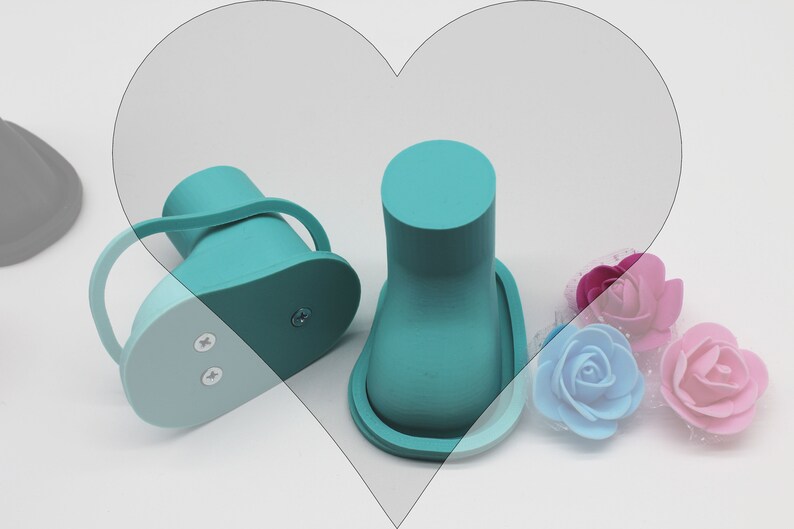 May include: Two teal blue baby shoes with a light blue sole. The shoes have a strap around the ankle and two small screws on the bottom. The shoes are sitting on a white surface with three artificial flowers.