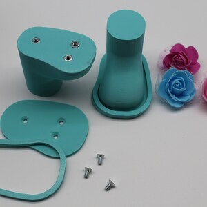 May include: A set of teal blue plastic parts for a 3D printed model, including two oval-shaped pieces with screw holes, a tall cylinder with a rounded top, and a smaller oval-shaped piece. There are also three silver screws.