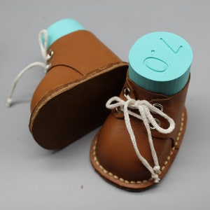 May include: Two brown leather baby shoes with white laces. One shoe has a turquoise blue block with the number "0" on it.