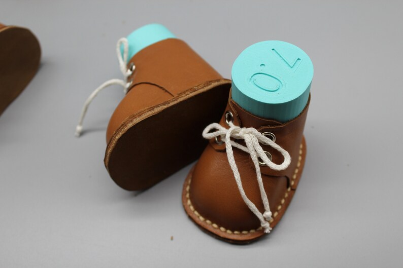 May include: Two brown leather baby shoes with white laces. One shoe has a turquoise blue block with the number "0" on it.
