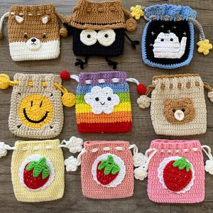 Peut inclure: Collection de neuf pochettes à cordon faites à la main au crochet. Chaque pochette présente un design unique, notamment un ours, un visage souriant, un nuage et des fraises. Les pochettes sont de différentes couleurs, dont le marron, le noir, le jaune, le rose et l'arc-en-ciel.