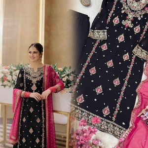 May include: A black embroidered formal outfit with a pink dupatta. The dress features detailed gold and pink embroidery on the neckline, sleeves, and hem. The ensemble includes matching black trousers and embellished shoes.