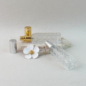 Refillable perfume atomizer bottles with removed caps, silver and gold pump designs, flat lay with flower decor.