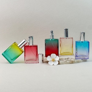 May include: Five rectangular glass perfume bottles in a row, each with a gradient color scheme. The colors include yellow to green, red, red to green, yellow, and blue to purple. Each bottle has a silver cap.