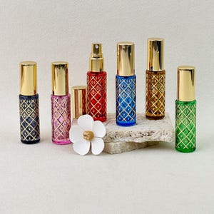 Pode incluir: Uma coleção de seis pequenos frascos de perfume de vidro com tampas douradas, cada um apresentando um padrão de treliça em forma de diamante com detalhes dourados. Os frascos são azul-escuro, rosa, vermelho, azul-brilhante, âmbar e verde.