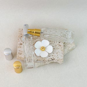 Close-up of refillable perfume spray bottles with gold and silver pumps, clear diamond-cut glass design with flower decor.