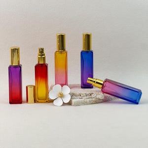 Gradient perfume bottles, including one lying on its side to show the sleek rectangular shape and gold spray pump.