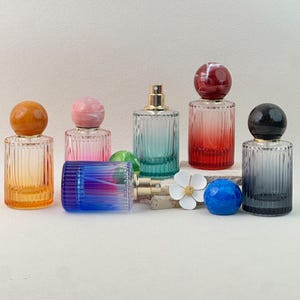 May include: Collection of decorative perfume bottles in various colors, including orange, pink, teal, red, and gray. Each bottle has a ribbed glass design and a spherical cap. Some bottles are upright, while others are lying down.