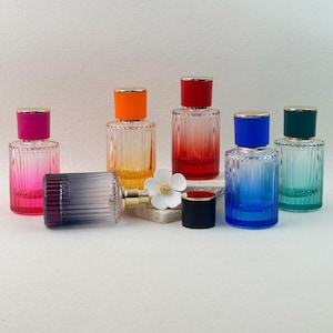 May include: A collection of colorful glass perfume bottles with gold-colored accents. The bottles are cylindrical with vertical ribbed detailing and are topped with caps in various colors, including pink, orange, red, blue, and green. One bottle is lying on its side.
