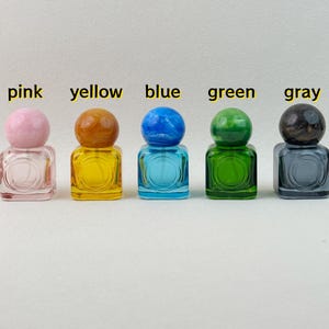 30ml square colored glass perfume bottles with matching marbled spherical caps, in pink, yellow, blue, green, gray on neutral background.