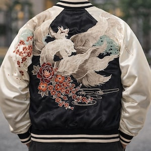 Pode incluir: Casaco bomber de cetim preto com mangas creme e um design bordado detalhado nas costas. O bordado apresenta uma criatura mítica branca com caudas fluidas, flores vermelhas e um design floral.