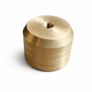 May include: A solid brass object with a threaded hole in the center. The object is cylindrical, composed of stacked, circular layers. The brass has a polished, metallic finish, and the object is set against a white background.