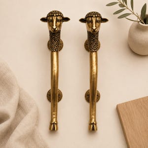 Peut inclure: Une paire de poignées de porte verticales en laiton avec une finition polie. Chaque poignée présente une tête de mouton détaillée sur le dessus, avec des détails de laine texturés sur le cou et un corps lisse et allongé se terminant par une base en sabot.