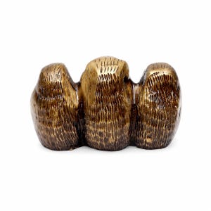 May include: A bronze-colored sculpture with a textured surface. The sculpture has three connected, rounded forms. The central form is slightly taller and more golden in color. The overall design is abstract and organic.