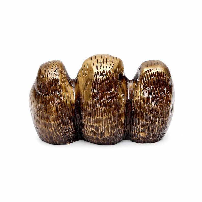 May include: A bronze-colored sculpture with a textured surface. The sculpture has three connected, rounded forms. The central form is slightly taller and more golden in color. The overall design is abstract and organic.
