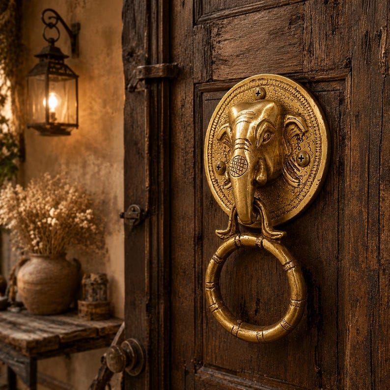 May include: A brass elephant head door knocker with a ring handle, mounted on a dark wooden door. The knocker features intricate details and a circular design. A vintage lantern hangs nearby.