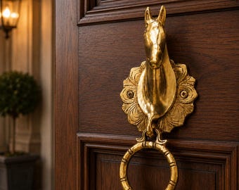 May include: A brass horse head door knocker with a ring handle, fixed to a dark brown wooden door. The horse head is surrounded by a decorative floral design.