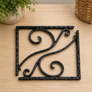 May include: A black metal shelf bracket featuring a square frame with a textured, hammered finish and two internal curved scrollwork supports. The bracket includes pre-drilled holes along the outer edges for mounting purposes.