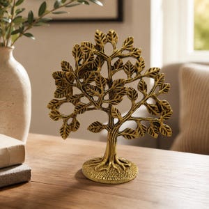 May include: A metallic gold-toned tree sculpture featuring a textured trunk, exposed roots at the base, and intricate branches adorned with numerous small, detailed leaves. The decorative object stands upright on a circular, textured base.