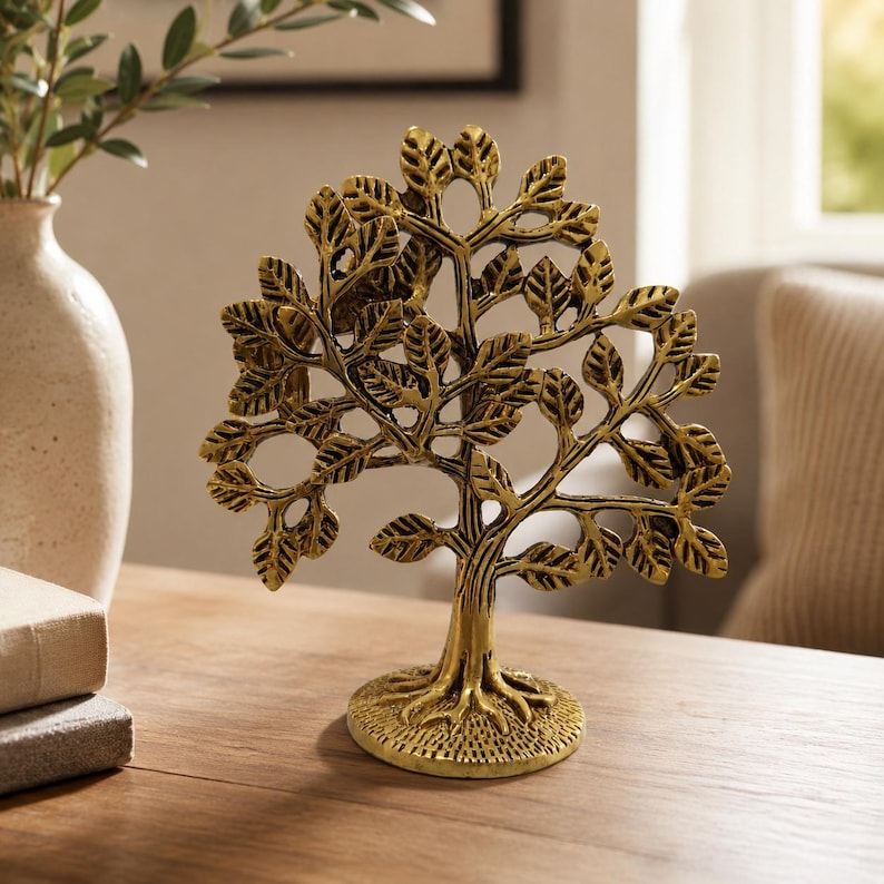 May include: A metallic gold-toned tree sculpture featuring a textured trunk, exposed roots at the base, and intricate branches adorned with numerous small, detailed leaves. The decorative object stands upright on a circular, textured base.
