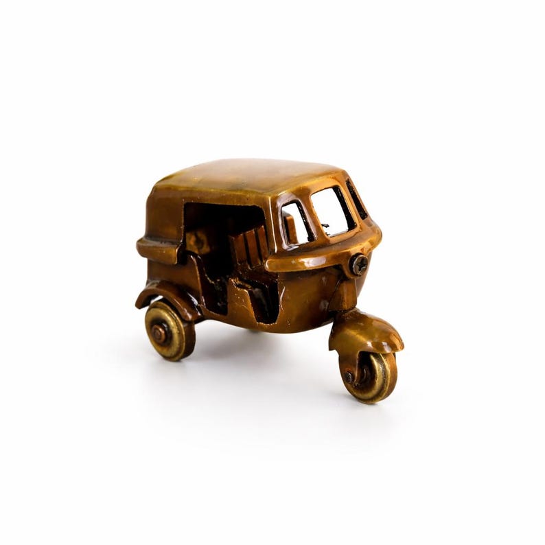 May include: A miniature bronze-coloured auto rickshaw with three wheels. The vehicle has a rounded roof, open windows, and detailed features. The front wheel is centered, and the side wheels are visible.