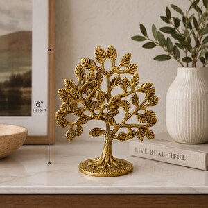 May include: A gold-colored metal tree sculpture with a textured trunk and numerous detailed leaves, standing on a circular base. A vertical measurement line indicates a total height of 6 inches for this decorative object.