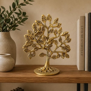 May include: A gold-colored metal sculpture of a tree with a textured trunk, spreading branches, and numerous detailed leaves. The tree stands on a circular base with a stippled surface texture, featuring a symmetrical design with open spaces.
