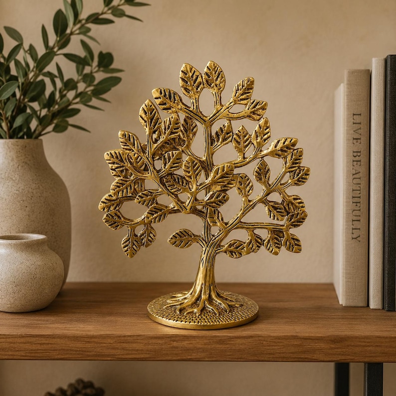 May include: A gold-colored metal sculpture of a tree with a textured trunk, spreading branches, and numerous detailed leaves. The tree stands on a circular base with a stippled surface texture, featuring a symmetrical design with open spaces.