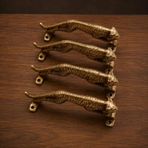 May include: Four brass tiger-shaped door handles arranged on a dark wood surface. Each handle is detailed with a textured finish, depicting a crouching tiger. The handles are approximately 8 inches long.