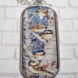 May include: A silver-toned pendant necklace with an oval-shaped pendant. The pendant features a detailed illustration of several small birds perched on branches with red berries against a blue and white background. The necklace has a delicate chain.