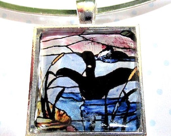 May include: A square silver pendant necklace featuring a stained glass style illustration of a black bird silhouette on a lake with cattails. The pendant has a glossy finish and is attached to a simple silver metal collar necklace band.