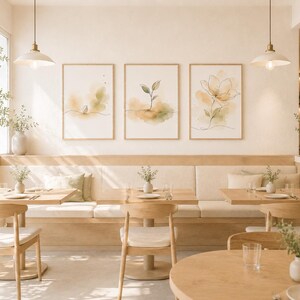 Peut inclure: Intérieur de café lumineux avec trois impressions botaniques aquarelles encadrées au-dessus d'une banquette intégrée. Des tables et des chaises en bois sont disposées dans l'espace, avec des vases décoratifs et des suspensions.
