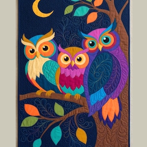 May include: A rectangular fabric wall hanging featuring three colorful owls perched on a brown tree branch against a dark blue background with a yellow crescent moon. The owls are rendered in shades of blue, orange, pink, and purple with intricate stitching.