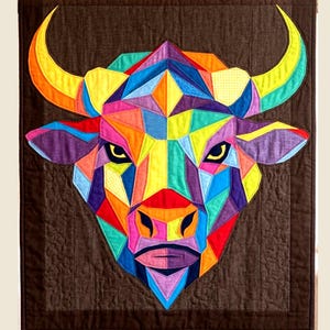 May include: A colorful geometric quilt featuring a bull's head. The bull is composed of various shapes and colors, including red, orange, yellow, green, blue, and purple. The background is a dark brown fabric with a quilted pattern.