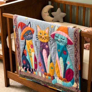 Puede incluir: Una colcha para bebé con tres figuras de gatos caprichosos con sombreros, cada uno con una combinación de colores única de naranja, azul y morado. La colcha se exhibe en una cuna de madera, con una almohada en forma de luna creciente y estrella en el fondo.