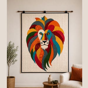 May include: A large, colorful quilt depicting a lion's head. The lion's mane is a vibrant mix of red, orange, yellow, green, and blue fabrics. The quilt is framed in black and hangs on a wall above a white armchair.