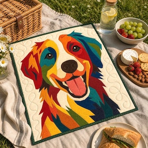 Puede incluir: Un edredón cuadrado y colorido con la cara de un perro sonriente. El pelaje del perro es un mosaico de rojo, naranja, amarillo, verde y azul. El edredón tiene un fondo crema con un borde verde. La lengua del perro es rosa.