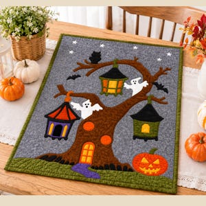 Puede incluir: Un tapiz rectangular de fieltro gris que presenta un árbol marrón con una puerta naranja brillante, tres linternas colgantes coloridas, dos fantasmas blancos, murciélagos negros y una calabaza tallada de color naranja bajo un cielo estrellado.