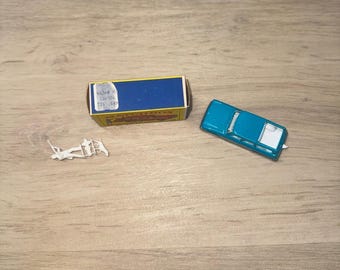 May include: A teal toy car with a white roof and a blue matchbox are on a light brown wooden surface. A small, white plastic toy is also present. The items are arranged on a light brown wooden surface.
