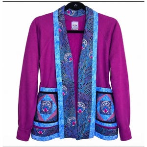 May include: A magenta-colored jacket with a unique design. The jacket features a patterned blue and purple fabric on the lapels and pockets, with a peacock feather motif. The pockets have a geometric design with pink accents.