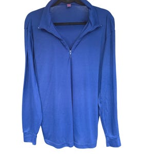 May include: A solid royal blue long-sleeve shirt featuring a quarter-zip closure at the collar. The garment has a pointed collar, long sleeves with cuffs, and a straight hemline. The fabric appears smooth and lightweight with a consistent color.
